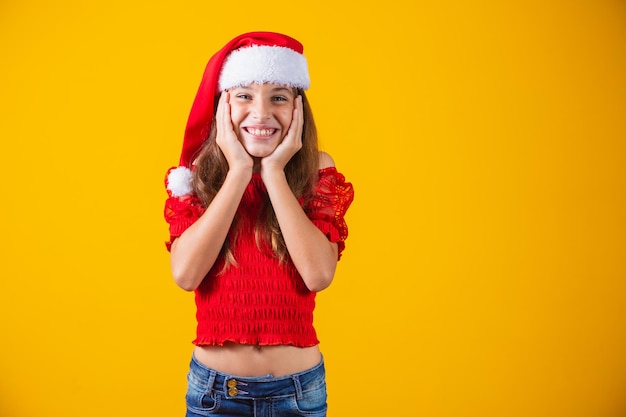 Portret van een Kaukasisch lachend meisje in een kerstmuts op een gele achtergrond. Kerstmis en geluk concept. Sluiten, ruimte kopiëren