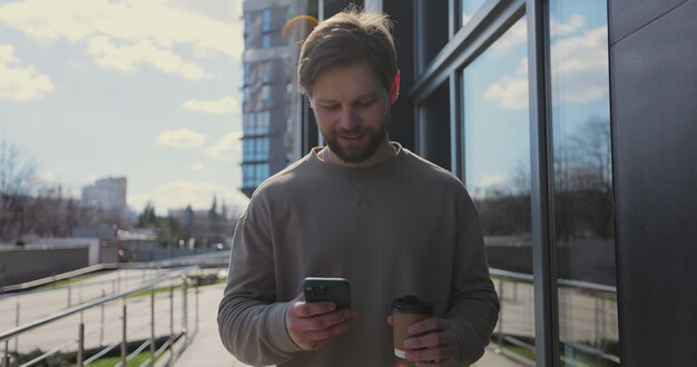 Portret van een kaukasische knappe man die drinkt om koffie te drinken en smartphone sociaal netwerken doorzoekt in stedelijke moderne straat mensen en communicatieconcept