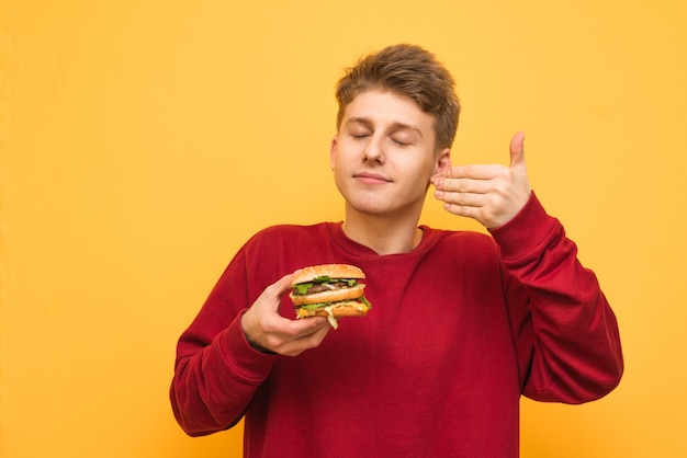 Portret van een kerel die een hamburger in zijn handen houdt en genietend van zijn gesloten ogen