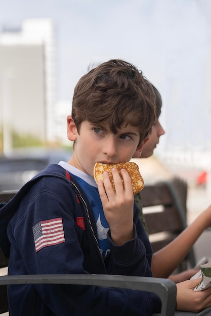 Portret van een kind dat verbijsterd of verrast wegkijkt terwijl hij een pannenkoek eet op een bankje in het park met zijn vriend ernaast