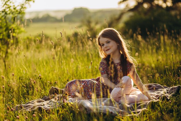 Portret van een klein babymeisje zittend op een plaid op picknick buiten bij zonsondergang