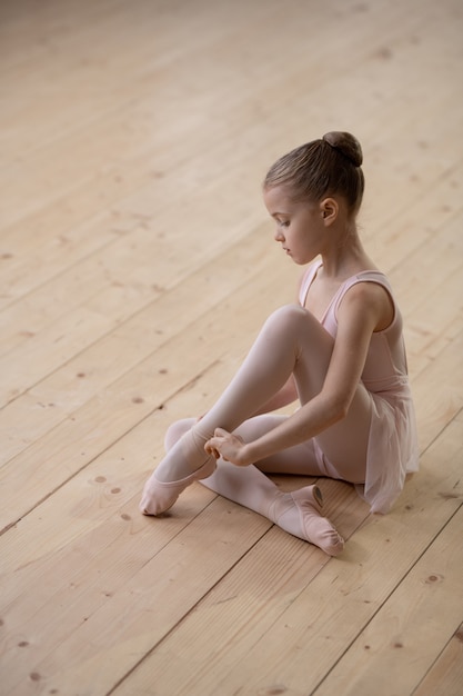Portret van een klein ballerinameisje dat naar de camera kijkt terwijl ze op de houten vloer in de dansclub zit