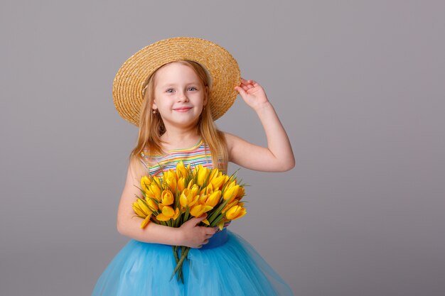 portret van een klein blond meisje in een strooien hoed met een boeket van Lentebloemen op een witte ruimte