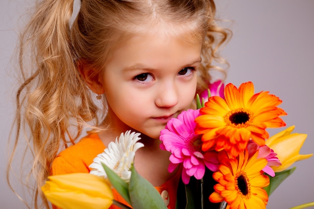 Portret van een klein blond meisje met een boeket van lentebloemen op een lichte muur