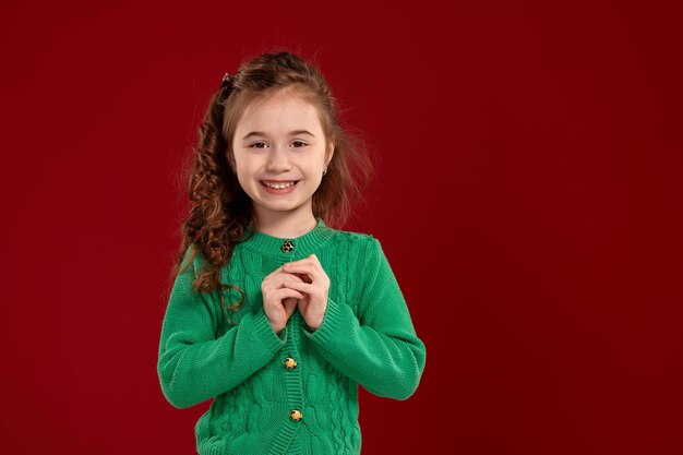 Portret van een klein brunette meisje met een lang, krullend haar poseren tegen een rode achtergrond.