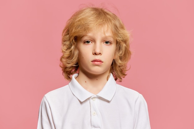 Portret van een klein jongenskind met blond krullend haar in een wit overhemd dat aandachtig naar de camera kijkt