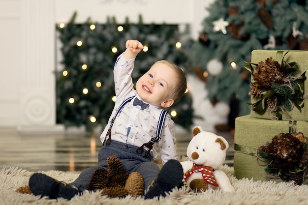 Portret van een klein jongensspel met denneappels dichtbij een Kerstboom. Kerst versiering. Vrolijk kerstfeest en een gelukkig nieuwjaar .