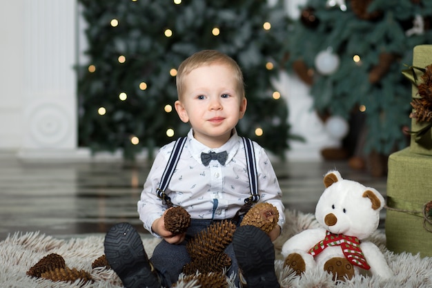 Foto portret van een klein jongensspel met denneappels dichtbij een kerstboom. kerst versiering. vrolijk kerstfeest en een gelukkig nieuwjaar .