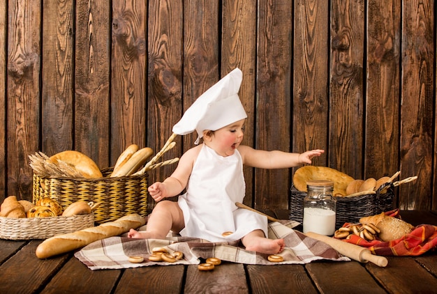 Portret van een klein kind in kokskleren onder bakkerijproducten op een houten achtergrond