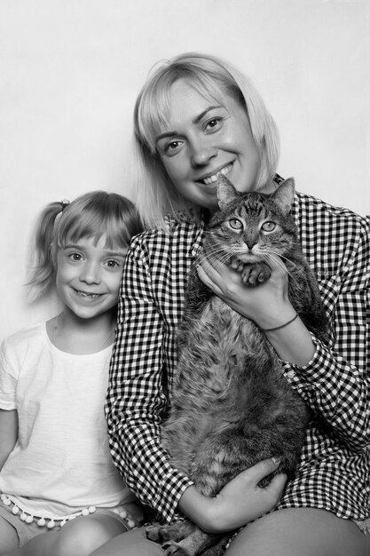 Portret van een klein lachend blond meisje met haar moeder die een gestreepte dikke kat met haar handen vasthoudt