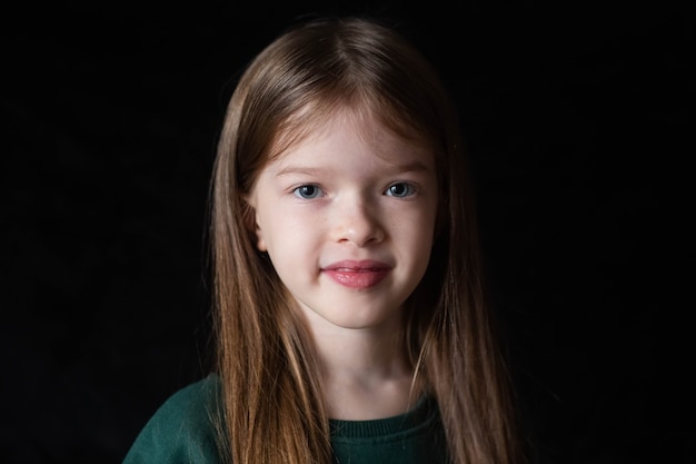 Foto portret van een klein lachend meisje met lang blond haar op zwart