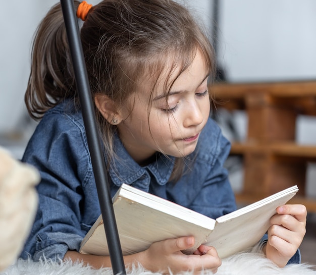 Portret van een klein meisje dat een boek leest dat op de vloer in de kamer ligt.