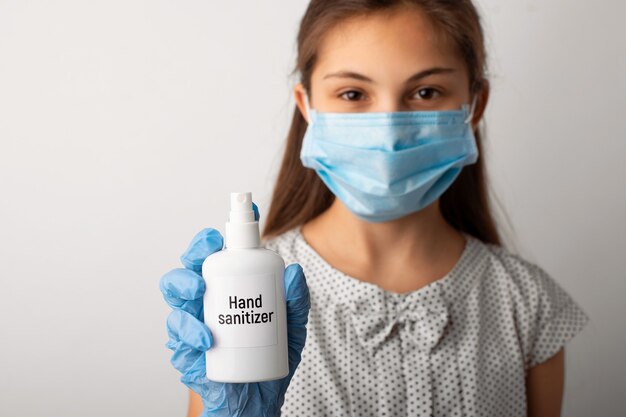 Portret van een klein meisje in medische masker en handschoenen die handdesinfecterend middel houden