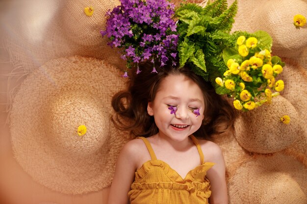 Portret van een klein meisje met bloemen op het gezicht liggend van strohoeden, zomer en reisgevoel concept.