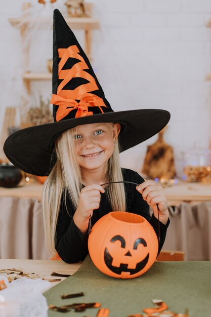 Portret van een klein meisje met lang haar in een heksenkostuum met een enorm Halloween-concept met heksenhoed