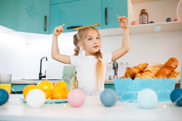 Portret van een klein meisje van 7 jaar oud zit in de keuken en speelt met broodstengels. Kind ontbijt in de keuken