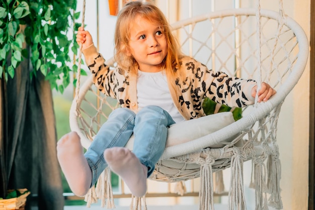 Portret van een klein meisje zittend in een hangstoel thuis op het balkon in de lente zomer zonsondergang