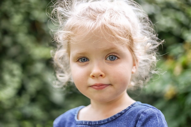 Portret van een klein mooi Europees meisje met blond krullend haar en blauwe ogen van 3 tot 4 jaar in een klassieke blauwe kleurjurk