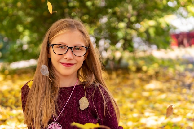portret van een klein mooi meisje in een bril met vallende gele herfstbladeren