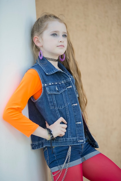 Portret van een klein roodharig meisje met lichte make-up in een denimvest.