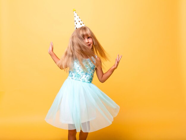 Portret van een klein schattig meisje in een feestelijke pet op een gele achtergrond. Verjaardag, vakantie.