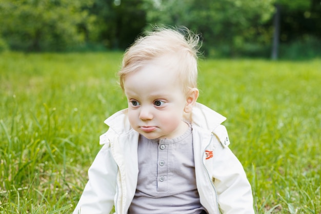 Portret van een kleine blanke blanke jongen. Op een zomerse dag zit een kind op het gras in een park.