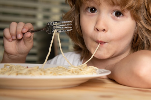 Portret van een kleine blonde jongen die pasta spaghetti eet close-up schattige kinderen worden geconfronteerd met een positief emotioneel kind