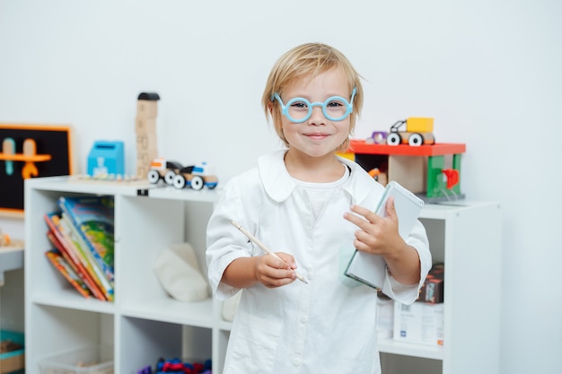 Portret van een kleine jongen die een dokter speelt met een speelgoedbril en een wit gewaad