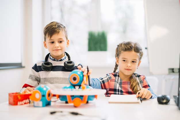 Portret van een kleine jongen die meisje het spelen met robotachtig stuk speelgoed bekijkt