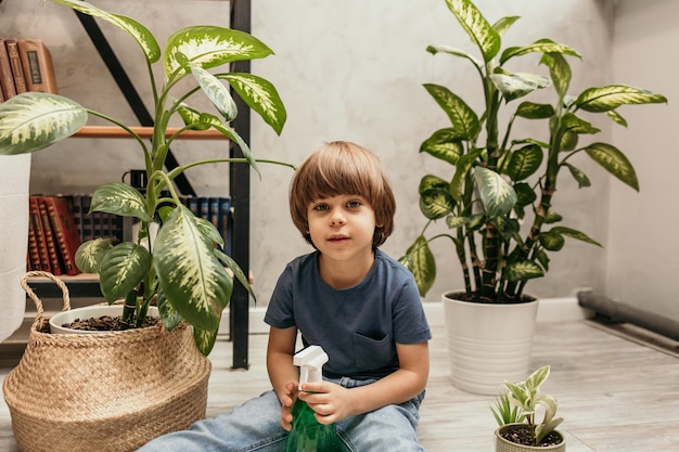 Portret van een kleine jongen die op de grond zit in een kamer met planten en een spuitpistool vasthoudt