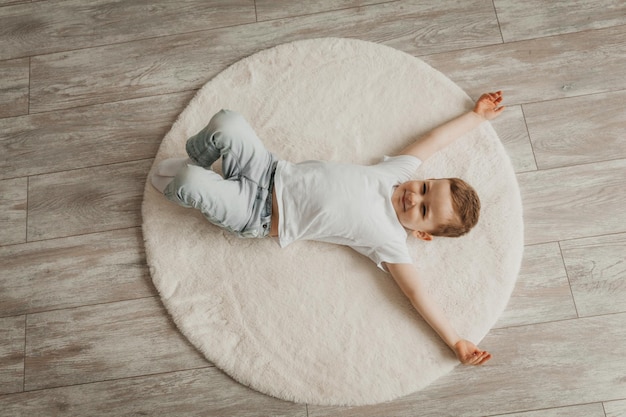 Portret van een kleine jongen die thuis op een tapijt vloerverwarming ligt