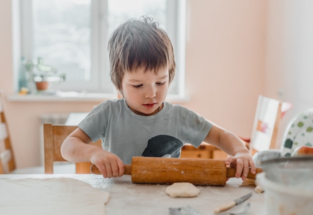 Portret van een kleine jongen in de keuken die deegroller gebruikt om het deeg voor koekjes voor te bereiden