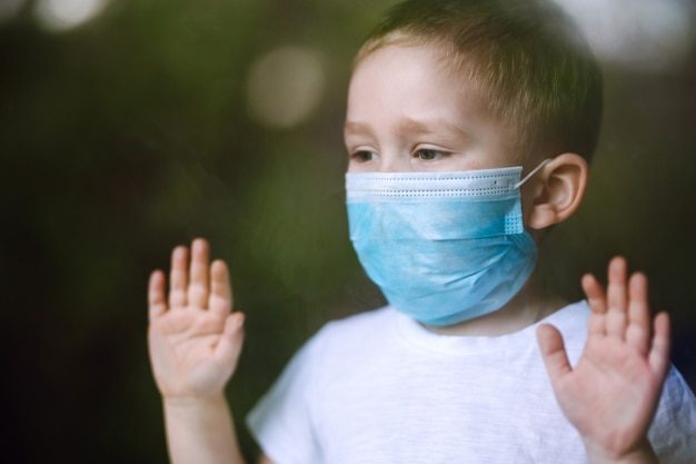 Portret van een kleine jongen met een medisch gezichtsmasker die naar de camera in de stad kijkt