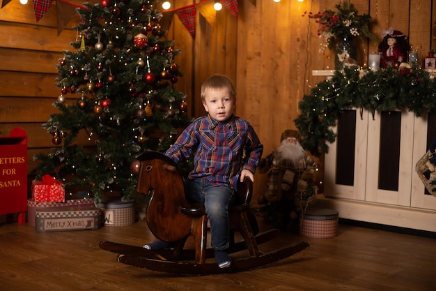 Portret van een kleine jongen op een hobbelpaard in de buurt van de kerstboom feestelijk ingericht huis