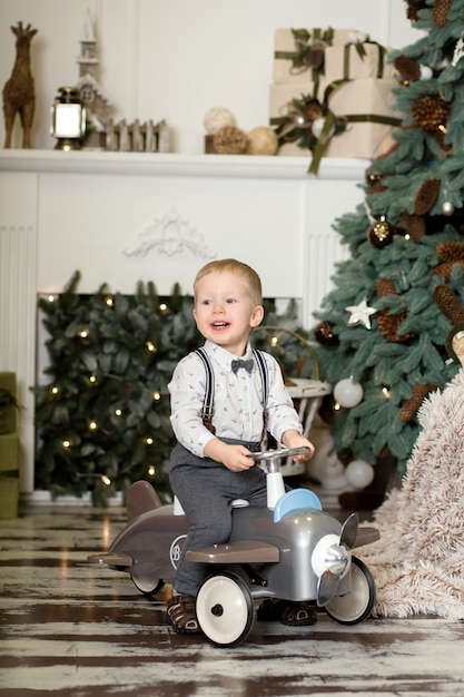 Portret van een kleine jongenszitting op een uitstekend stuk speelgoed vliegtuig dichtbij een Kerstboom