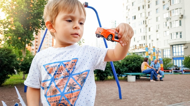 Portret van een kleine peuterjongen die met speelgoedauto's speelt op de speelplaats