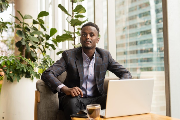 Portret van een knappe Afrikaanse zakenman die in de coffeeshop zit met een laptopcomputer