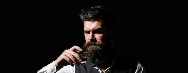 Portret van een knappe bebaarde in elegante smoking, drink cognac. Aantrekkelijke man met een whisky. Bebaarde man. Stijlvolle knappe man in pak drinken van glas cognac, cognac.