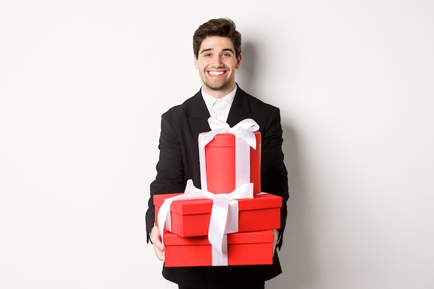 Portret van een knappe bebaarde man in trendy pak, met cadeaus voor het nieuwe jaar en glimlachend, voorbereide cadeautjes, staande op een witte achtergrond.