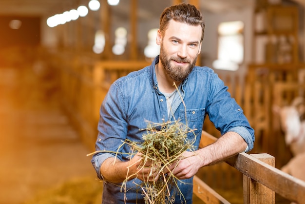 Portret van een knappe boer die met hooi in de geitenschuur staat. natuurlijke melkproductie en landbouw