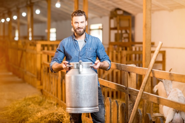 Portret van een knappe boer die met retro melkcontainer in de geitenschuur staat. Natuurlijke melkproductie en landbouw