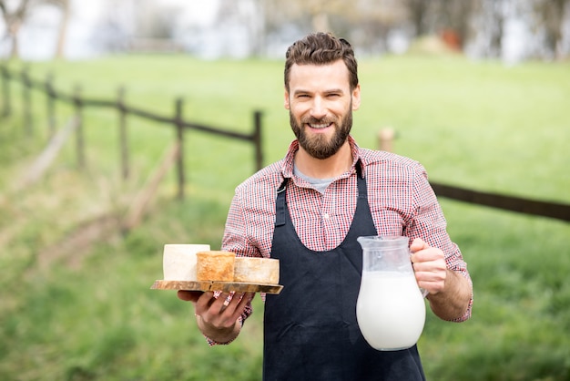 Portret van een knappe boer in schort met geitenkazen en melk buiten op de achtergrond van de groene weide