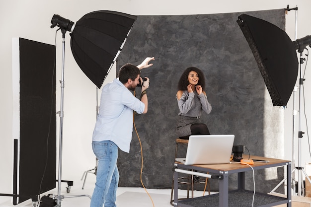 Portret van een knappe fotograaf die een brunette vrouwelijk model schiet met professionele camera en softbox in de studio