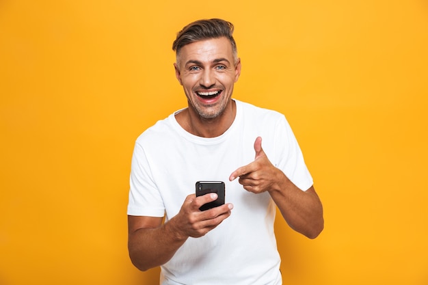 Portret van een knappe gelukkig man poseren geïsoleerd op gele muur met behulp van mobiele telefoon.
