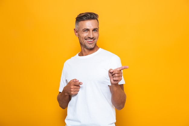 Portret van een knappe gelukkig opgewonden man poseren geïsoleerd op gele muur wijzend.