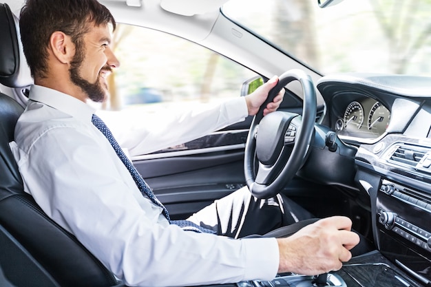 Portret van een knappe, gelukkige zakenman die in zijn auto rijdt