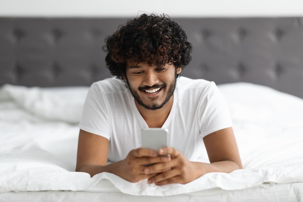 Portret van een knappe hindoe-man die op bed ligt met een telefoon