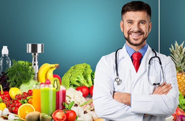 Portret van een knappe jonge dokter die staat met gekruiste armen op de achtergrond van groenten en fruit