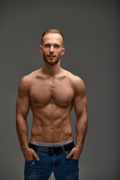 Portret van een knappe jonge kerel model een shirtless met een gespierd gezond lichaam pronken met zijn biceps spieren op een grijze achtergrond
