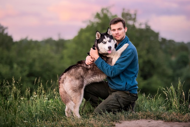 Portret van een knappe jonge man en zijn geliefde hond Siberische Husky knuffelen in de natuur